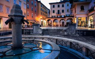 Fontana in una piazza storica al tramonto, con edifici colorati.