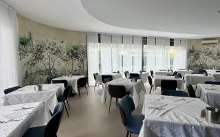 Ristorante elegante con tavoli apparecchiati e murale botanico.
