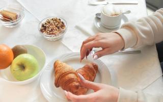 Colazione elegante con croissant, frutta e cappuccino su tavola apparecchiata.