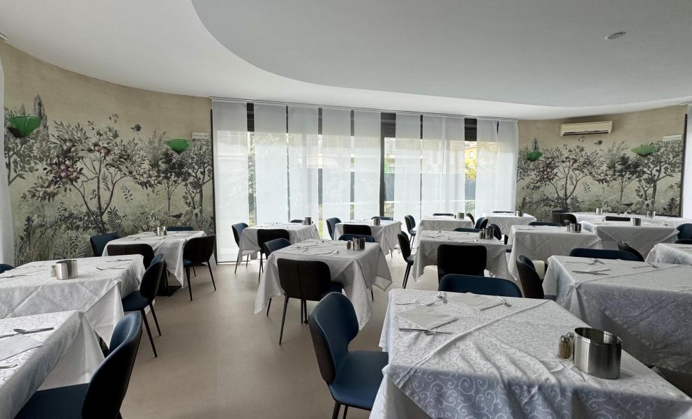 Ristorante elegante con tavoli apparecchiati e murale botanico.