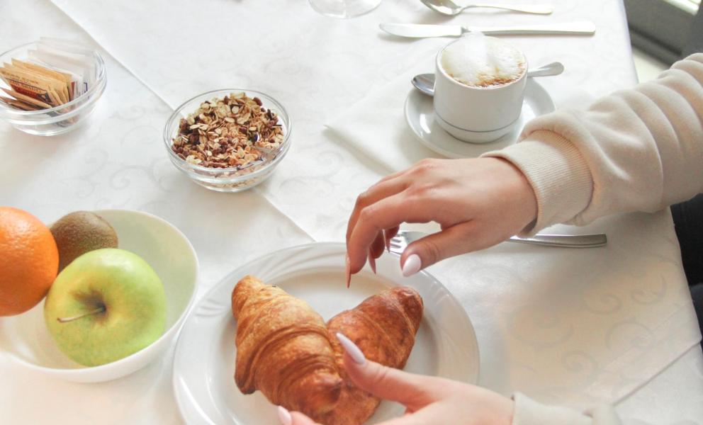 Colazione elegante con croissant, frutta e cappuccino su tavola apparecchiata.