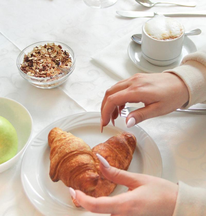 Breakfast with croissant, fruit, and cappuccino on a set table.